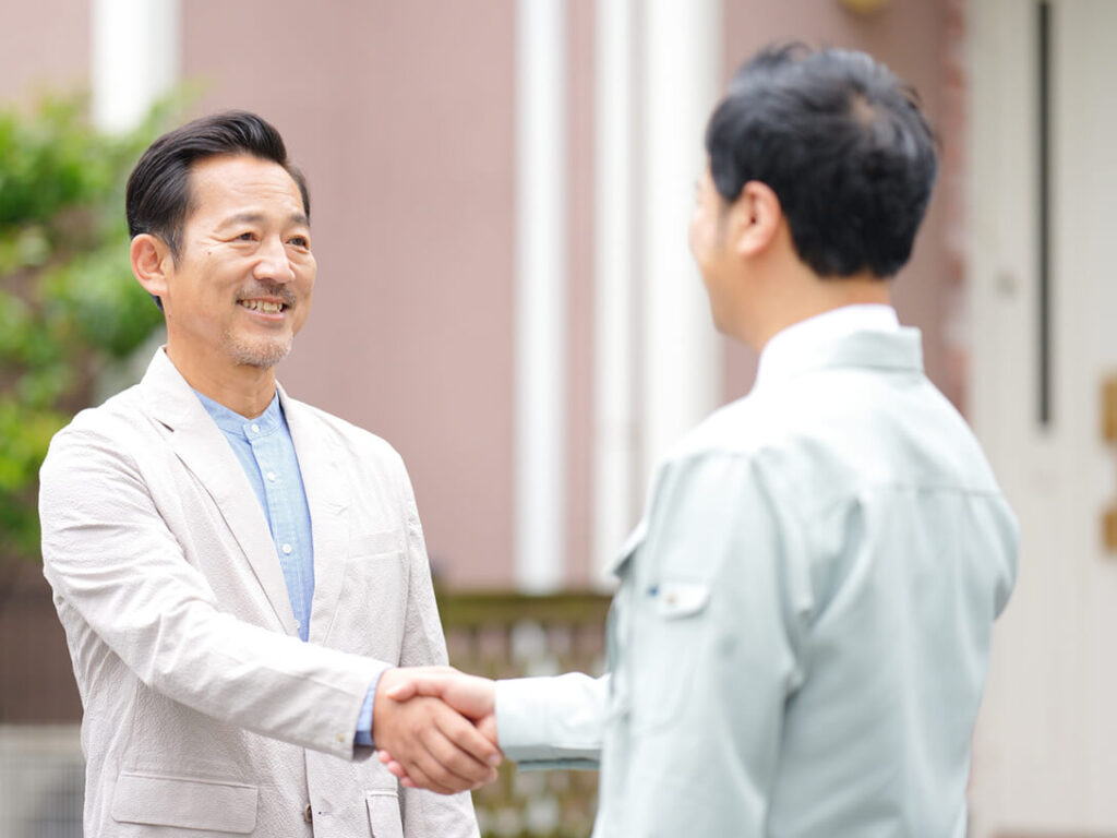 屋外で笑顔の男性と作業着姿の職人が握手している様子。