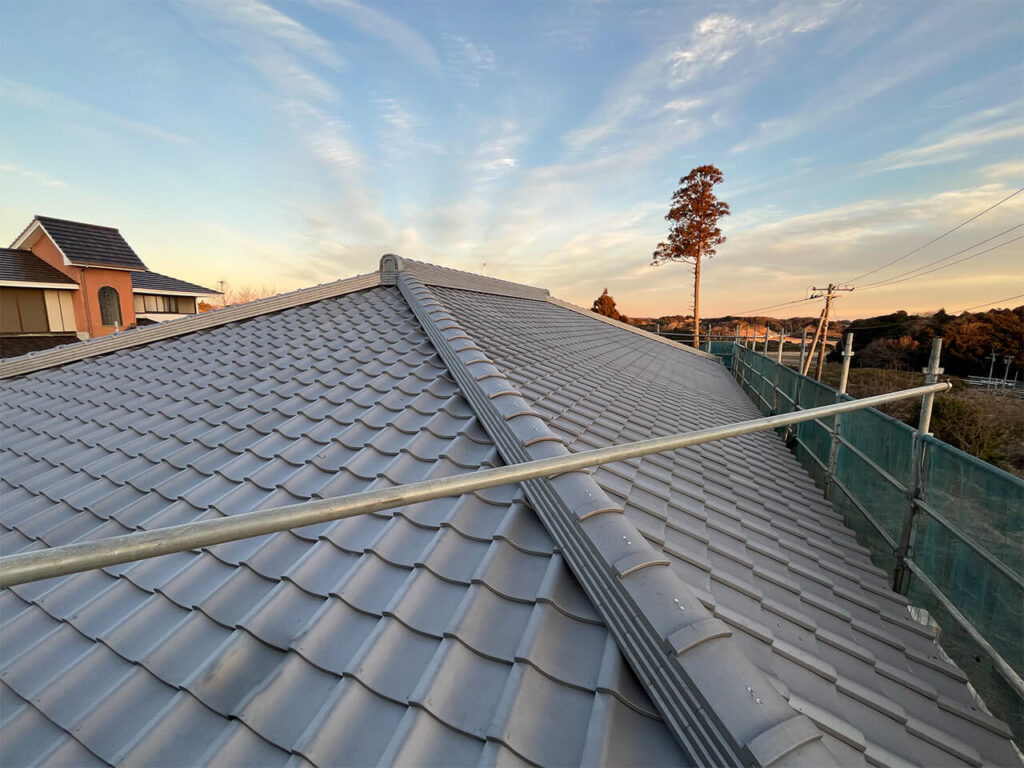 足場の設置された現場で、夕日に照らされる銀色の和瓦屋根